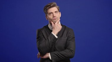 Mavi arka planda etrafa bakınan bir iş adamı. Resmi takım elbiseli, dalgın bir adam. Yakışıklı erkek manken cevabı. Yüksek kalite 4k