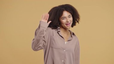 Dost canlısı genç Afrikalı Amerikalı kadın el sallıyor ya da selam, kaos, adios. Ayrılıyorum, kameraya hoşça kal de. Bej renkli stüdyo arka planda güzel bir bayan. Yüksek kalite 4k