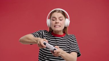 Kırmızı stüdyo arka planında joystick izole edilmiş video oyunu oynayan güzel genç bir kadın. Modern teknolojiyi kullanarak. E-spor, hobi, akış