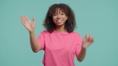 Dost canlısı genç Afrikalı Amerikalı kadın el sallıyor ya da selam, kaos, adios. Ayrılıyorum, kameraya hoşça kal de. Mavi stüdyo arka planındaki güzel bayan. Yüksek kalite 4k