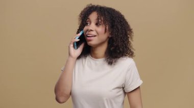 Çekici genç Afrikalı kız telefonla konuşuyor, gülümsüyor. Öğrenci bayan bej arka planda güler. Ergen, akıllı telefon görüşmesi yapıyor. Yüksek kalite 4k görüntü