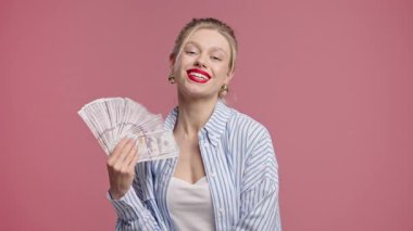 Nakit parası olan zengin, heyecanlı bir kadın. Pembe duvarda Amerikan Doları banknotları. İkramiye, kazanç, zafer, kazanan piyango, maaş sembolü. Yüksek kalite 4k