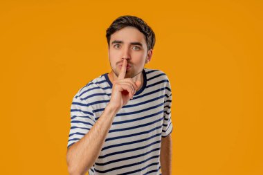 Sessiz, sessiz, komplo, sessiz, söylenti konsepti olan yakışıklı bir adam. Gülümseyen adam parmaklarını dudağında tutuyor, sarı stüdyo geçmişi var. Yüksek kalite