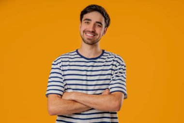 Slav görünümlü neşeli genç adam canlı sarı arka planda duruyor, sıcak bir gülümseme ve pozitif, enerjik bir portre oluşturuyor..