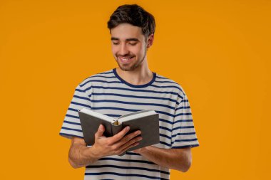 Yakışıklı okuyucu, parlak sarı arkaplana karşı duruyor, elinde tuhaf, meşgul bir ifadeyle kitabı tutuyor ve okuyor. Zeki çocuk. Keşif, öğrenme, entellektüel merak, kaliteli zaman geçirme