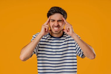 Baş ağrısı, kan basıncı, stüdyo portresi olan genç bir adam. Kafasında elleri olan, izole edilmiş sarı arka planı olan beyaz bir öğrenci. Sorunlar, migren semptomları, hastalık. Yüksek kalite