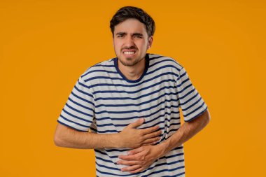 Karın ağrısı yüzünden karnını ellerinle sıkan bir adam. Yetişkin adam mide ağrısı çekiyor. Sağlık hizmetleri, sindirim sistemi, gıda zehirlenmesi veya bağırsak gazı konsepti