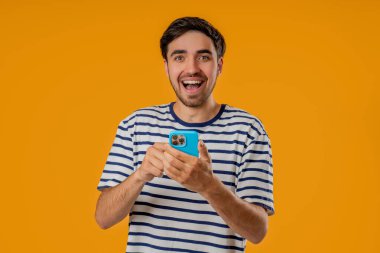 Cep telefonuyla internette sörf yapan yakışıklı bir erkek. Sarı arka planda gülücük ve neşe dolu bir adam. Teknoloji, başarı, mutluluk, sosyal ağ konsepti. Yüksek kalite