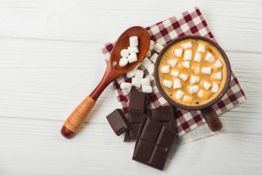 Bir fincan kremalı sıcak kakao ve beyaz masada çikolata.