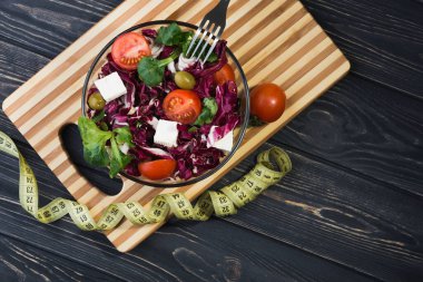 Domatesli cam kasede taze salata, peynirli peynir ve ahşap masada yeşil yapraklar. diyet kavramı