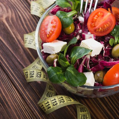 Domatesli cam kasede taze salata, peynirli peynir ve ahşap masada yeşil yapraklar. diyet arkaplanı