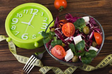 Domatesli taze salata, peynirli peynir ve ahşap arka planda yeşil yapraklar.