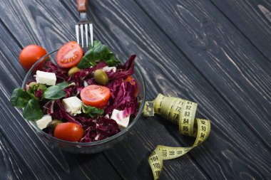 Domatesli cam kasede taze salata, peynirli peynir ve ahşap masada yeşil yapraklar. diyet arkaplanı