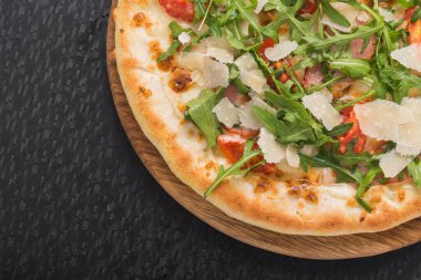 Tahta üzerinde domates, peynir, pastırma ve roka olan lezzetli bir pizza. siyah arkaplan