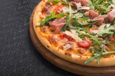 Siyah mutfak masasında prosciutto ve rogula soslu İtalyan pizzası.