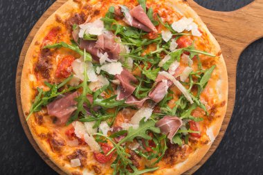 Siyah mutfak masasında prosciutto ve rogula soslu İtalyan pizzası.