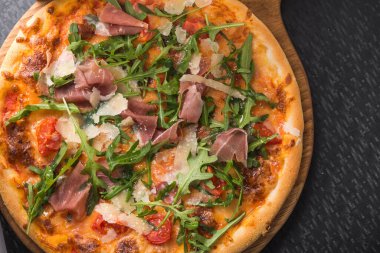 Siyah mutfak masasında prosciutto ve rogula soslu İtalyan pizzası.