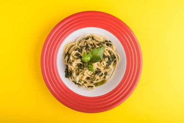 Kırmızı tabakta parmesanlı ve fesleğenli İtalyan spagettisi, sarı masa.