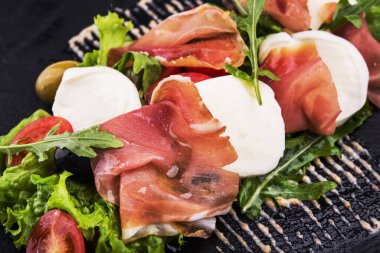 Prosciutto, mozzarella, taze domates ve roka tabağında salata.