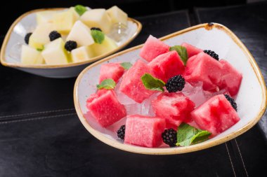 Kesilmiş kırmızı karpuz, içinde nane ve siyah bir arkaplanda buz var.