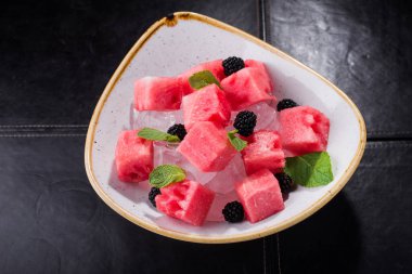 Kesilmiş kırmızı karpuz, içinde nane ve siyah bir arkaplanda buz var.