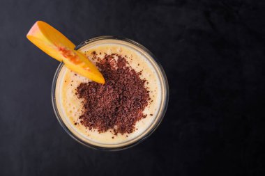Bir bardak şeftalili smoothie, siyah arka planda çikolata parçaları.