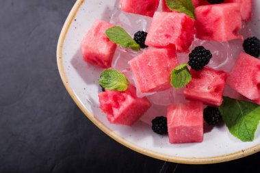 Kesilmiş kırmızı karpuz, içinde nane ve siyah bir arkaplanda buz var.