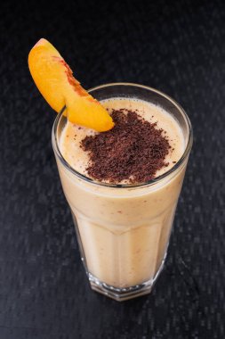 Bir bardak şeftalili smoothie, siyah arka planda çikolata parçaları.