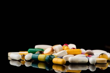 Siyah arkaplanda ayna yansıması olan renkli ilaç kapsülü