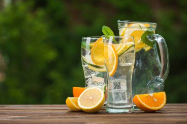 Portakallı mojito bardakta ve tahta masada nane yaprağı var. 