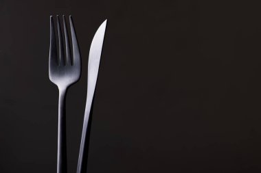 Siyah arkaplanda siyah çatal ve bıçak var.