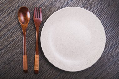 Tahta masa üzerinde çatal ve kaşıkla boş beyaz tabak. tepeden görünüm