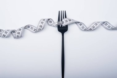 Diyet kavramı, siyah çatal ve ölçüm bandı beyaz arka planda izole edildi