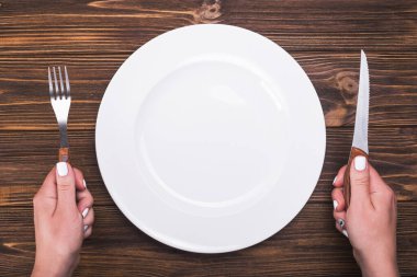 Çatal ve bıçaklı kadın eli. Tabağın üstü, ahşap masa.