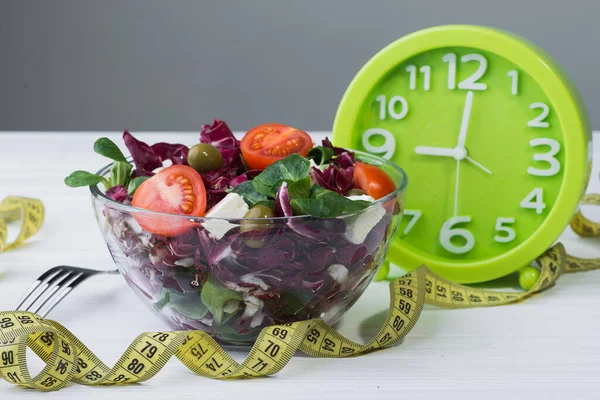 Domatesli cam kasede taze salata, peynirli peynir ve ahşap masada yeşil yapraklar. diyet arkaplanı