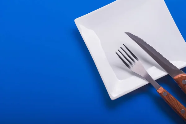 ナイフで白いプレートを空にし 青いテーブルの上にフォーク 上から見ると — ストック写真