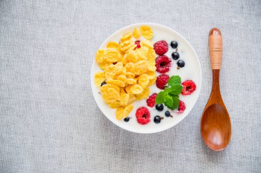 Kahvaltıda mısır gevreği, yoğurt ahududu ve mutfak masasında yeşil nane şekeri.