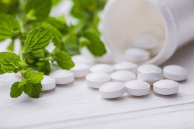 Beyaz arka planda bitkisel yeşil yapraklı beyaz haplar. 