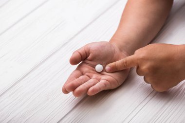 Tahta arka planda beyaz tıbbi haplar olan çocuk eli. Çocuk tedavisi