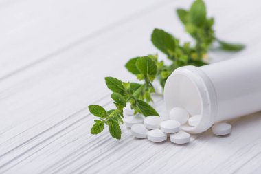 Beyaz arka planda bitkisel yeşil yapraklı beyaz haplar. 