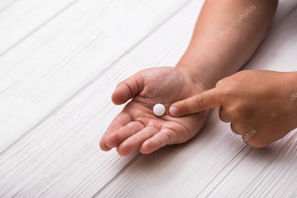Child hand with white medical pills on wood background. Children treatment