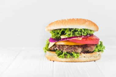 Beyaz ahşap masada domates ve soğanlı klasik hamburger.