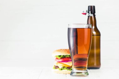 Klasik hamburger ve bira bardağı, ahşap beyaz masada şişe.