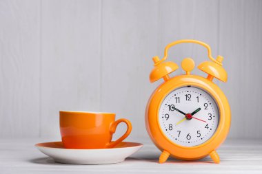 Bir fincan kahve, mutfak masasında çalar saat, ahşap arka plan.