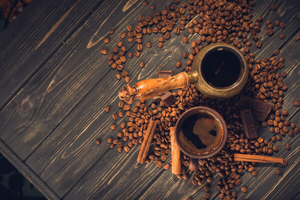 Old coffee cup and turk with roasted beans on a wooden table. Vintage aroma concept on dark background.