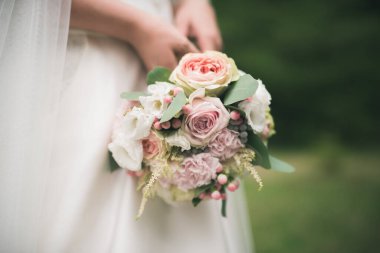 Beyaz elbiseli güzel gelin elinde bir buket gül tutuyor. Romantik bir düğün günü