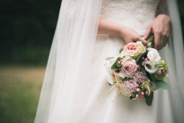 Beyaz elbiseli güzel gelin elinde bir buket gül tutuyor. Romantik bir düğün günü