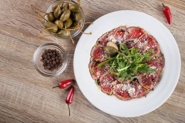 Biftek carpaccio roka ve ahşap bir masada kapari.