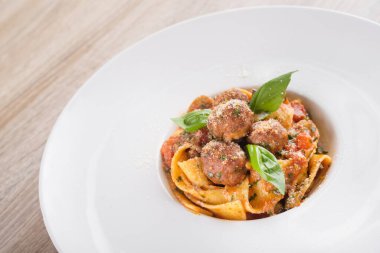 Beyaz tabakta köfteli taze makarna, ahşap masa.