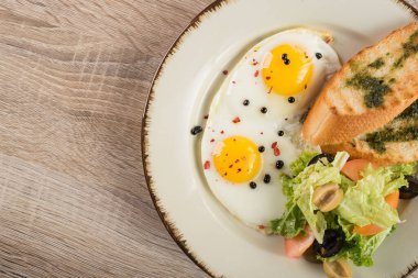 Ahşap arka planda kızarmış yumurta, kızarmış ekmek ve sebze. Restorandaki masada kahvaltı.